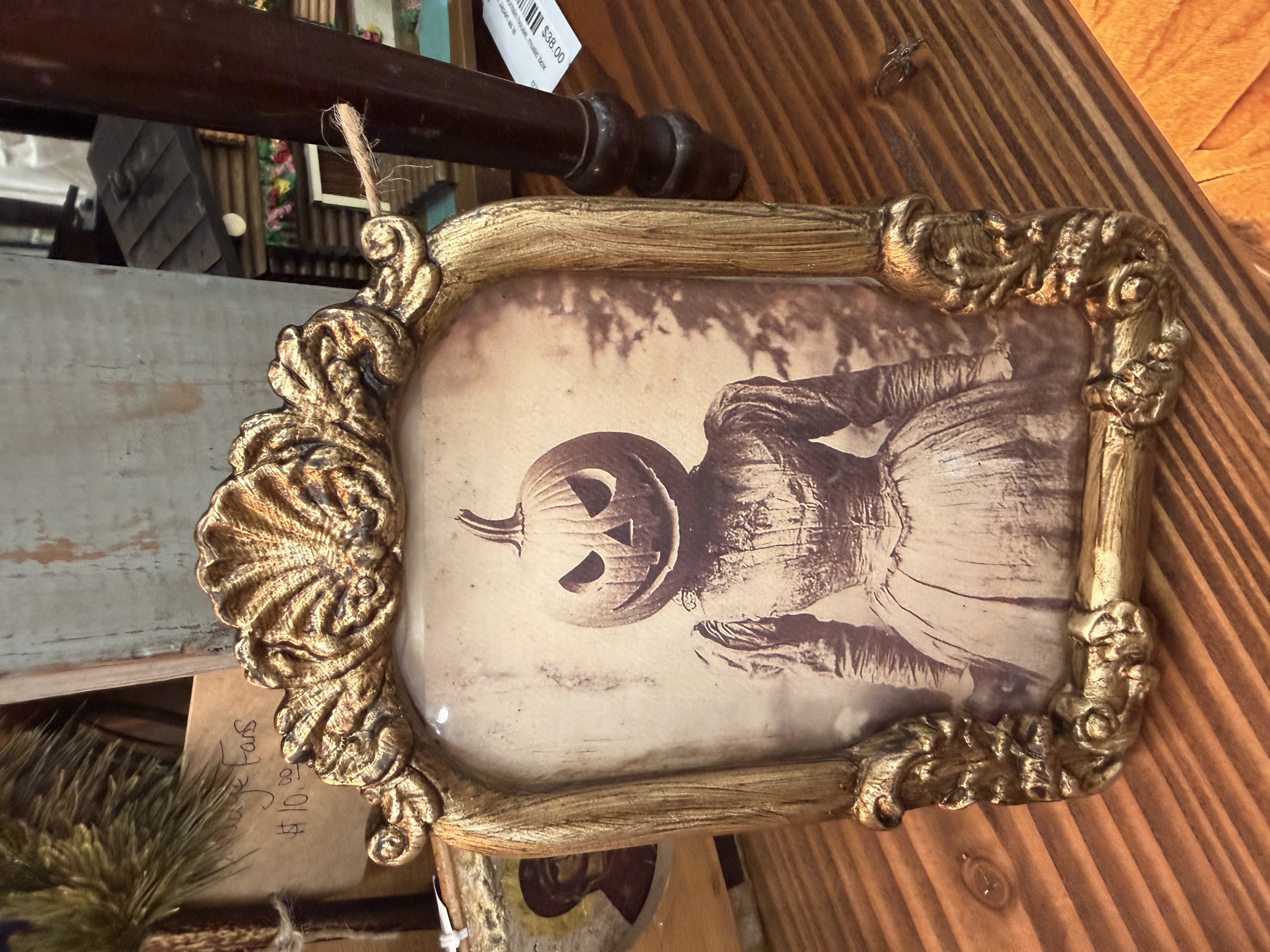 An ornate gold baroque frame holding a sepia Victorian photograph of a woman with a carved jack-o-lantern head